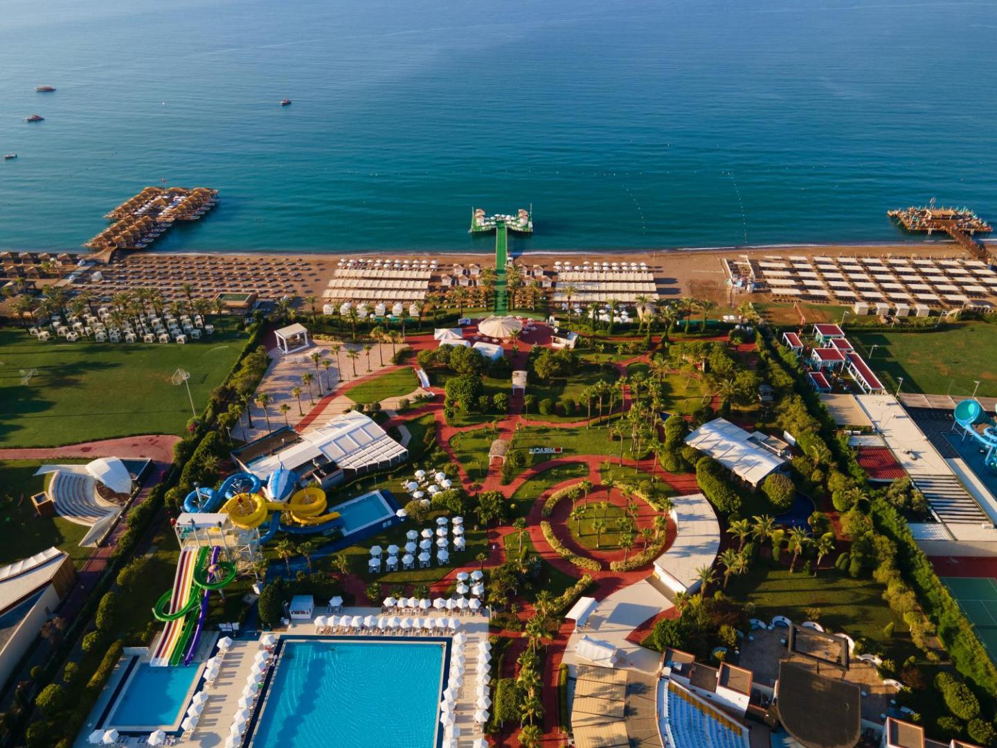 Miracle Resort Hotel Antalijā skats no putna lidojuma uz plašo teritoriju, akvaparku, dārzu un privāto pludmali ar piestātni Vidusjūras krastā