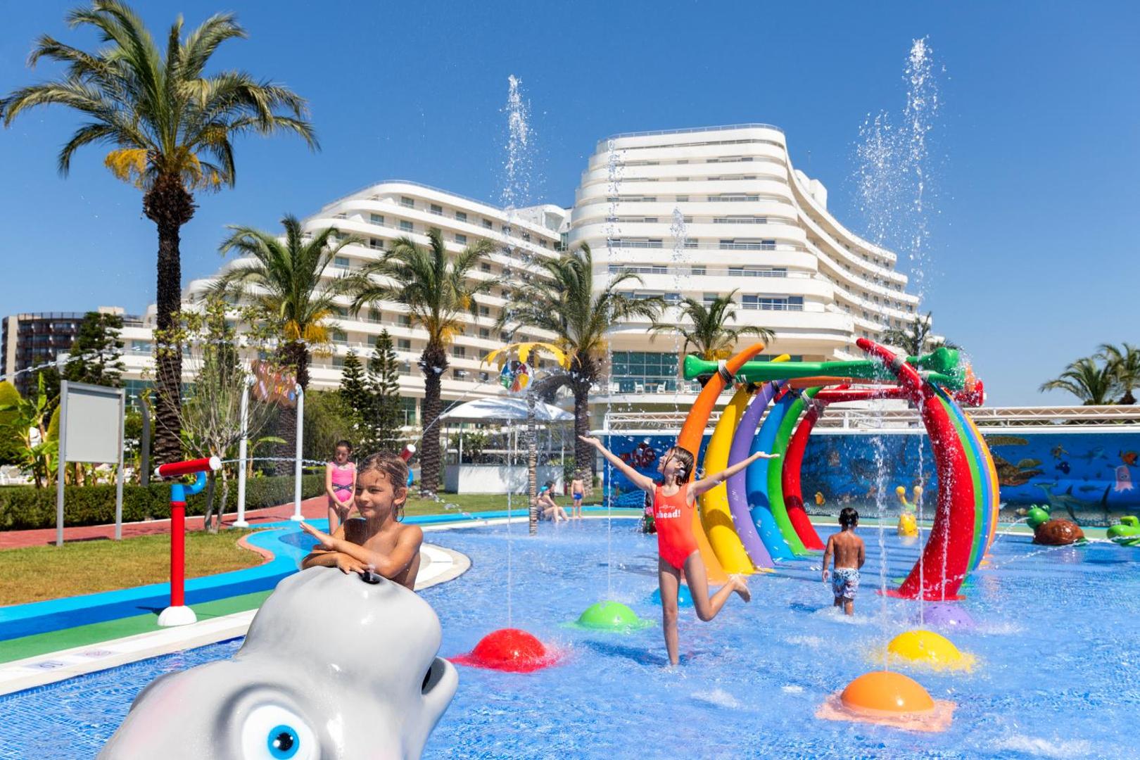 Miracle Resort Hotel bērnu akvaparks ar krāsainiem ūdens tuneļiem un strūklakām piekrastē — fonā redzama viesnīcas galvenā ēka