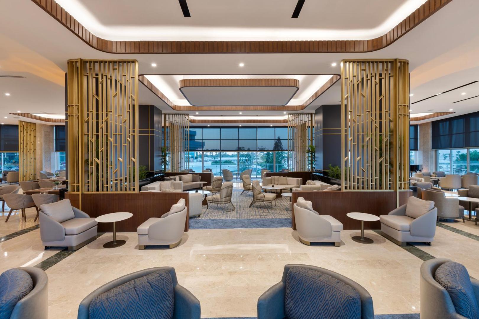 Miracle Resort Hotel plašais un modernais lobby bārs ar ērtiem atpūtas krēsliem, zelta elementiem un lieliem logiem Antalijā