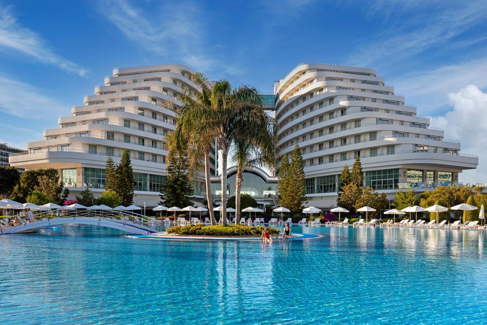 Miracle Resort Hotel galvenā ēka un lielais āra baseins Antalijā, Turcijā — saulaina diena ar palmām un atpūtas krēsliem pie ūdens