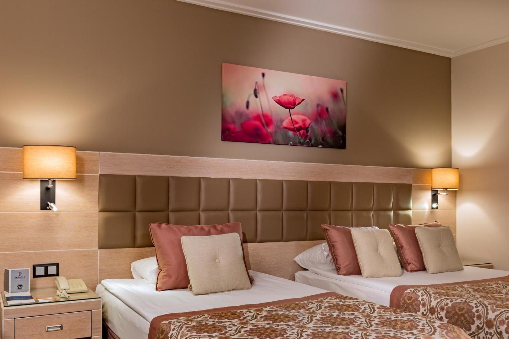 Miracle Resort Hotel numura interjera detaļa ar divām gultām, dekoratīviem spilveniem un ziedu gleznu pie sienas.