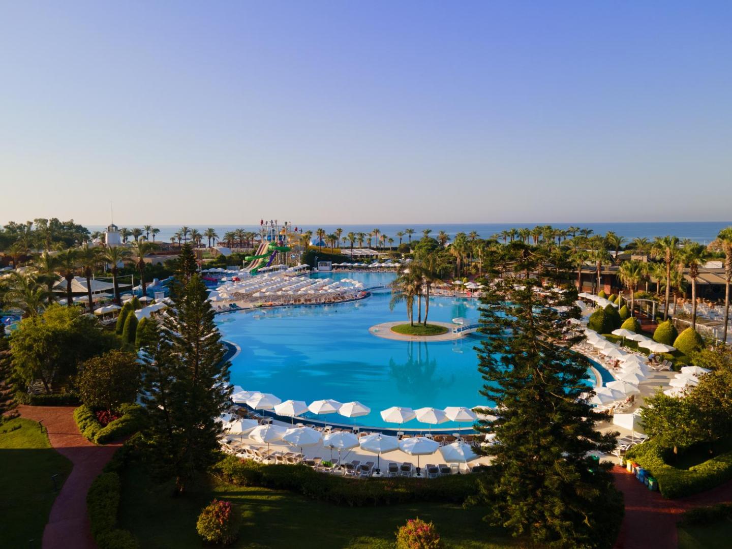 Aerofoto skats uz Miracle Resort Hotel baseinu kompleksu un akvaparku Antalijā — dārza ainava un Vidusjūras piekraste fonā