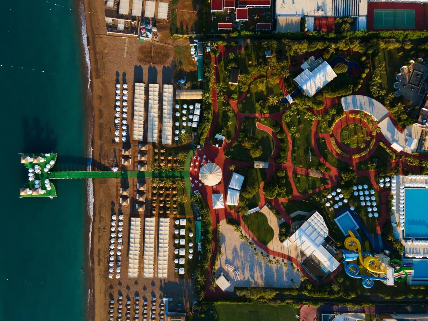 Miracle Resort Hotel pludmales zona no augšas ar saulessargiem, piestātni jūrā un dārza celiņiem, kas ved uz krastu