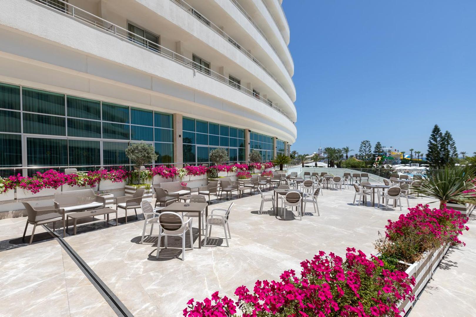 Miracle Resort Hotel āra terase ar galdiņiem, krēsliem un ziedošām puķēm pie viesnīcas galvenās ēkas
