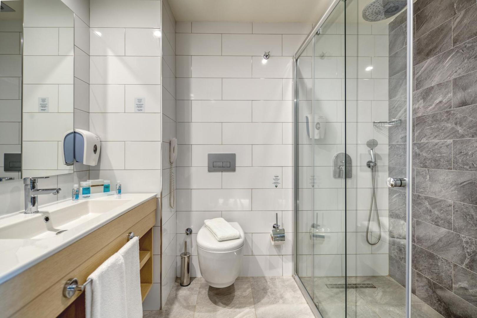 Gaiša Numa Bay Exclusive Hotel vannas istaba ar flīzētu sienu, plašu spoguli un stikla dušas zonu gaišos toņos