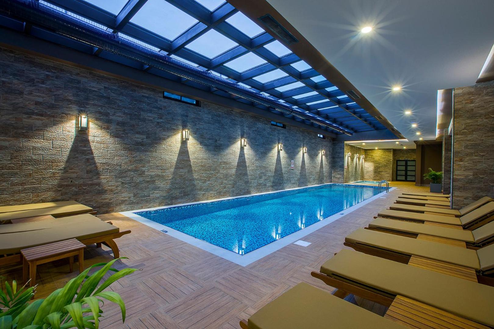 Numa Bay Exclusive Hotel iekštelpu baseins ar stikla jumtu, akmens sienām un ērtiem zviļņiem spa zonā