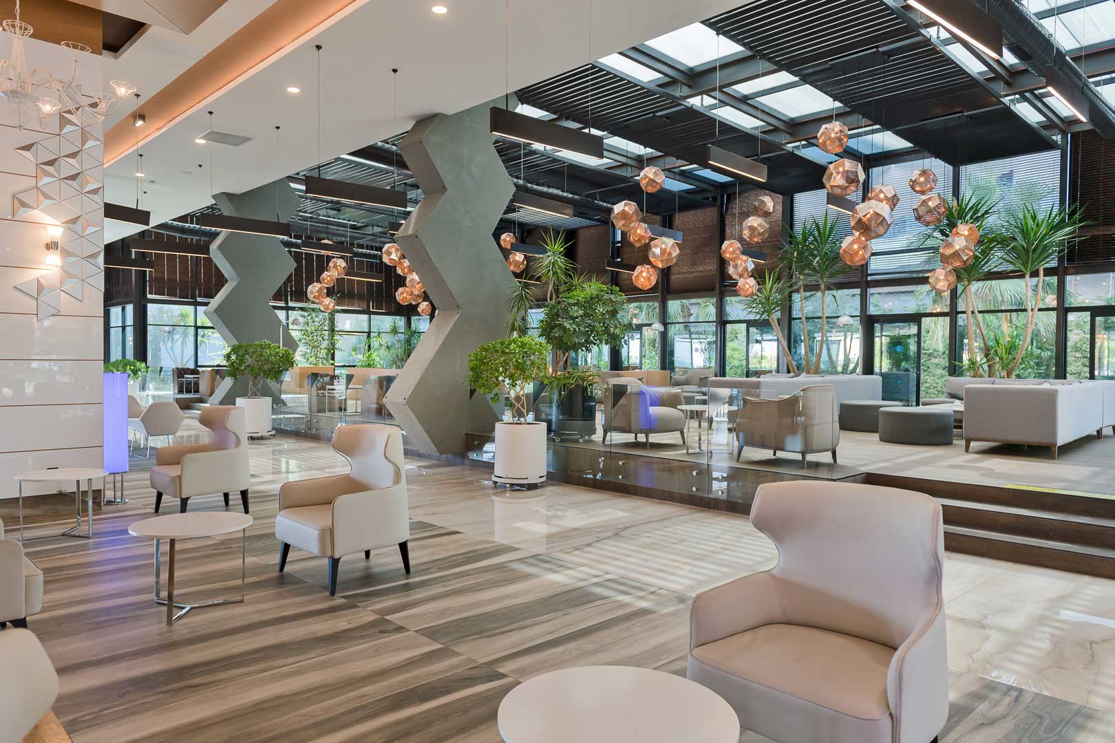 Gaiša Numa Bay Exclusive Hotel vestibila zona ar augstiem griestiem, dizaina gaismekļiem un dekoratīviem telpaugiem dienas gaismā