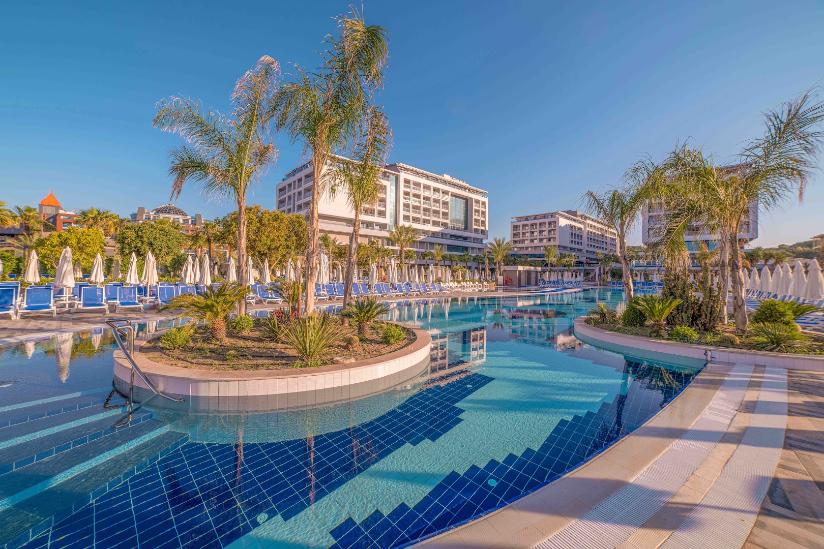 Numa Bay Exclusive Hotel lielais āra baseins ar palmām un viesnīcas ēku fonā saulainā pēcpusdienā Alanjā