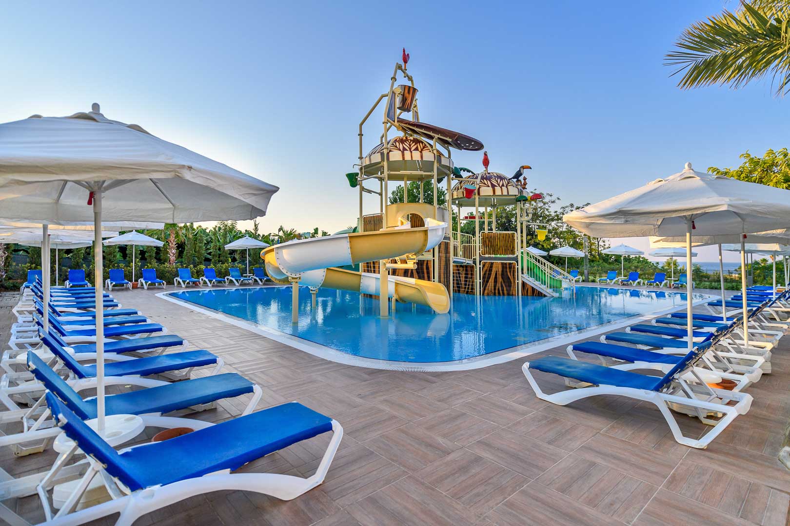 Numa Bay Exclusive Hotel bērnu baseins ar krāsainiem slidkalniņiem, ūdens atrakcijām un sauļošanās krēsliem zem saulessargiem Turcijas piekrastē