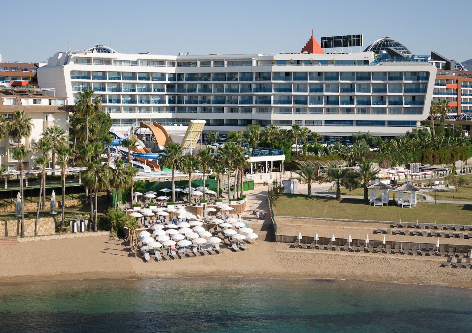 Selene Beach and Spa Hotel skats no jūras puses — privātā smilšu pludmale ar saulessargiem, ūdens slidkalniņi un viesnīcas fasāde