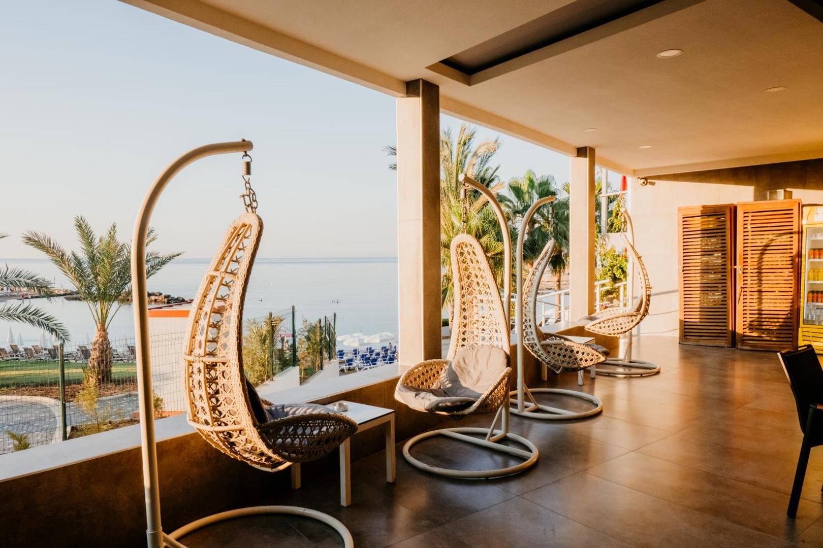 Selene Beach and Spa Hotel terase ar moderniem iekaramajiem krēsliem un skatu uz Vidusjūru saulrieta gaismā