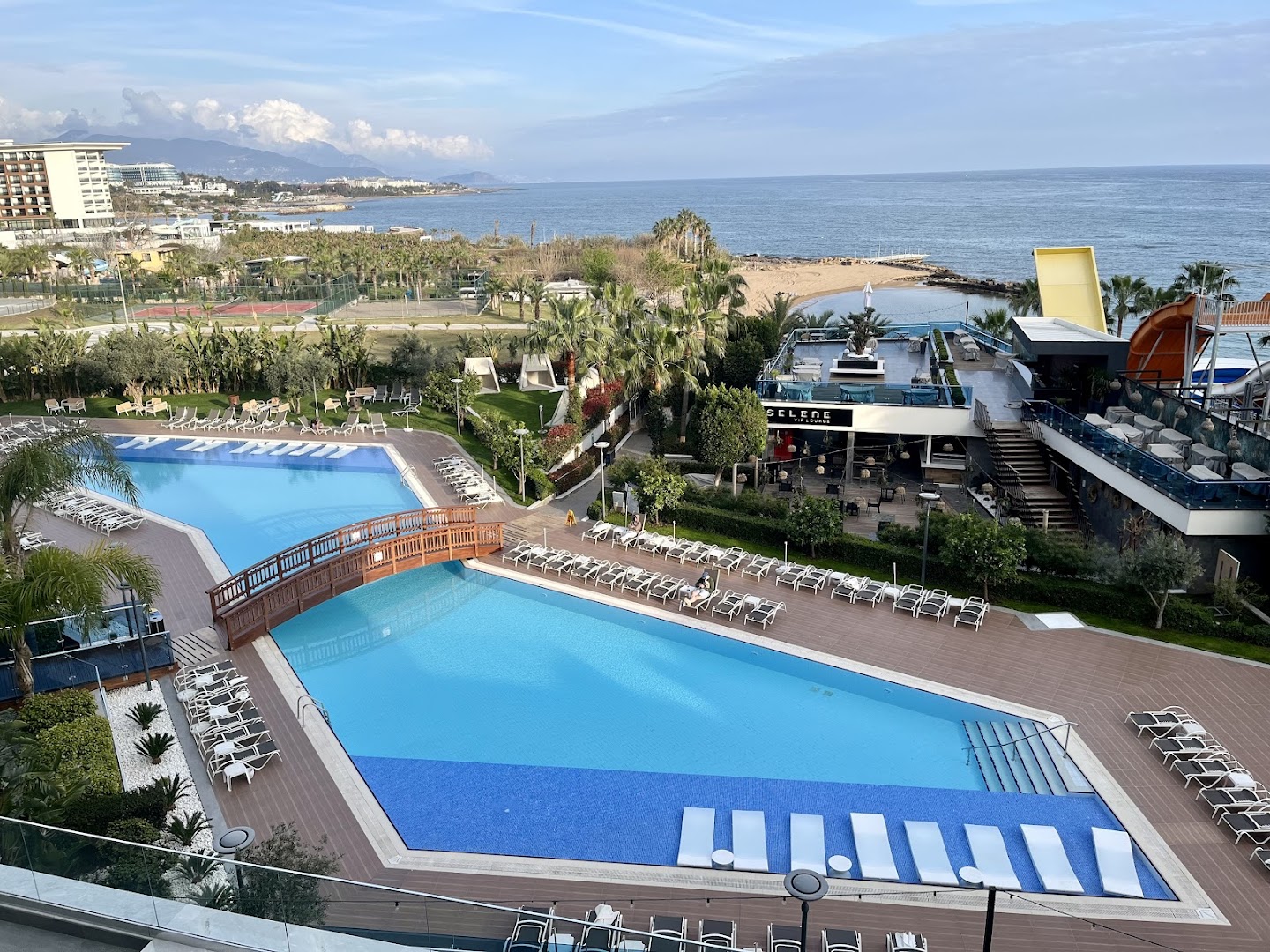 Selene Beach and Spa Hotel centrālais baseins ar koka tiltiņu, sauļošanās krēsliem un skatu uz jūru Alanjas piekrastē