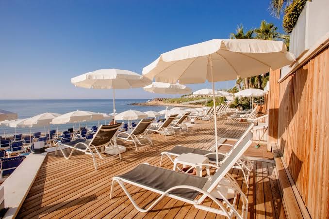 Selene Beach and Spa Hotel privātā pludmales terase ar koka klāju, sauļošanās krēsliem un saulessargiem pie Vidusjūras