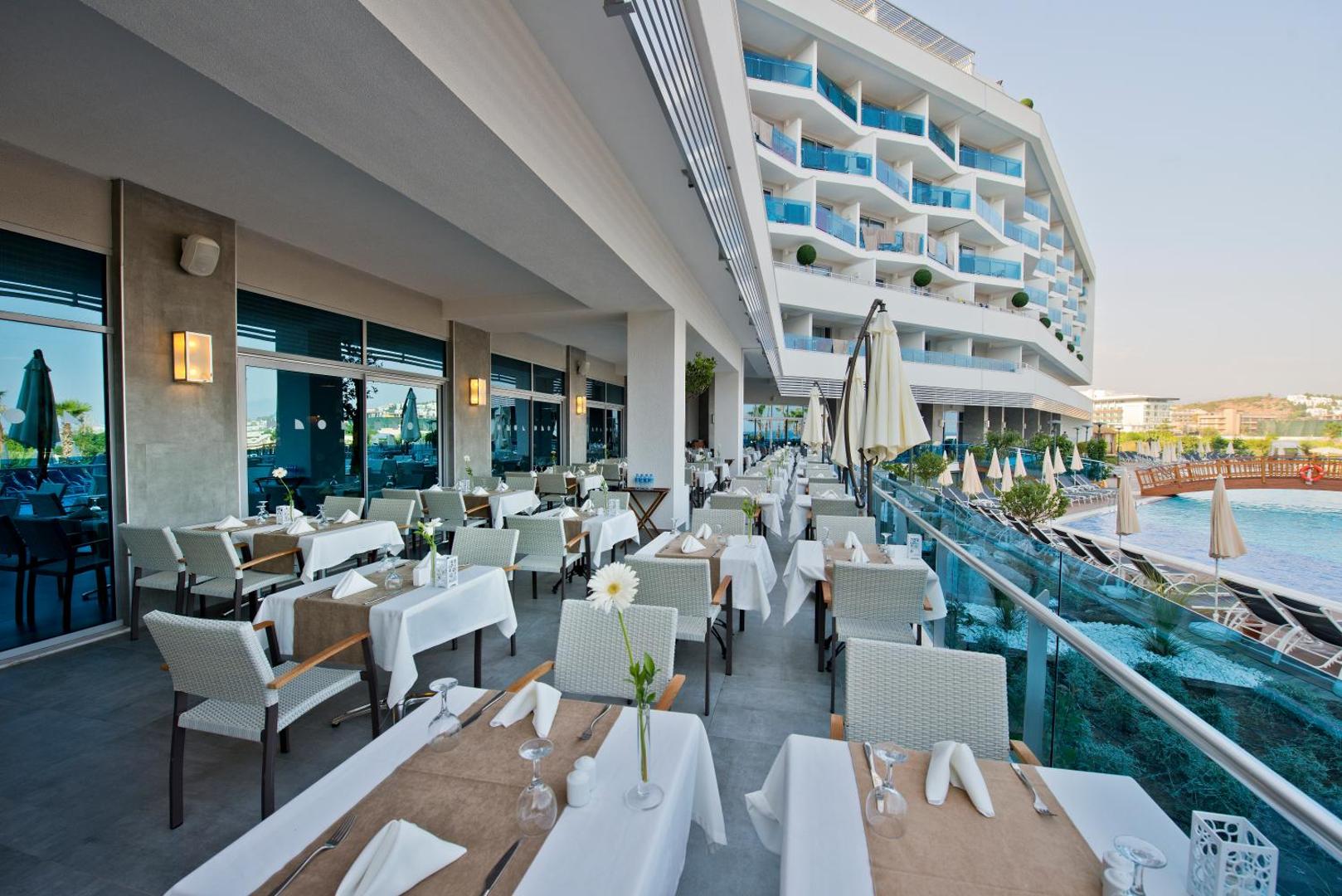 Selene Beach and Spa Hotel restorāna āra terase ar skatu uz baseinu un viesnīcas korpusu — eleganti klāti galdi vakariņām piekrastē