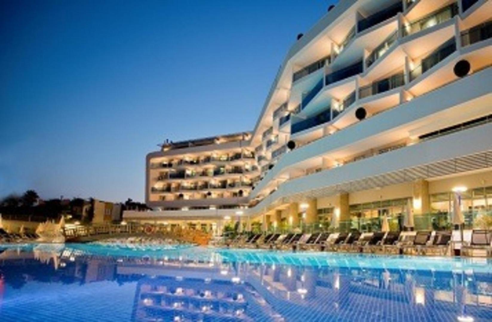 Selene Beach and Spa Hotel modernā fasāde un izgaismotais āra baseins vakarā Alanjas reģionā, Turcijā — luksusa atpūtas zona ar sauļošanās krēsliem
