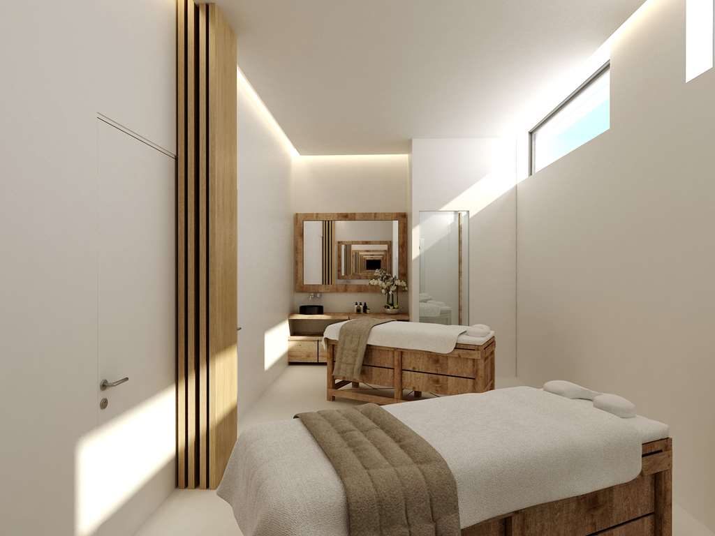 Gaišs un mūsdienīgs masāžas kabinets Radisson Beach Resort Larnaca spa centrā ar diviem procedūru galdiem un koka detaļām.