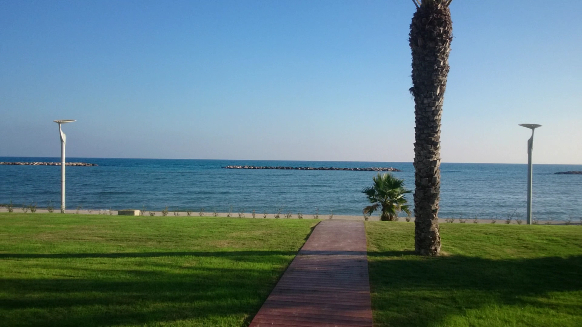 Radisson Beach Resort Larnaca koka laipa ved caur zaļu zālienu uz smilšu pludmali un zilo Vidusjūru Kipras piekrastē