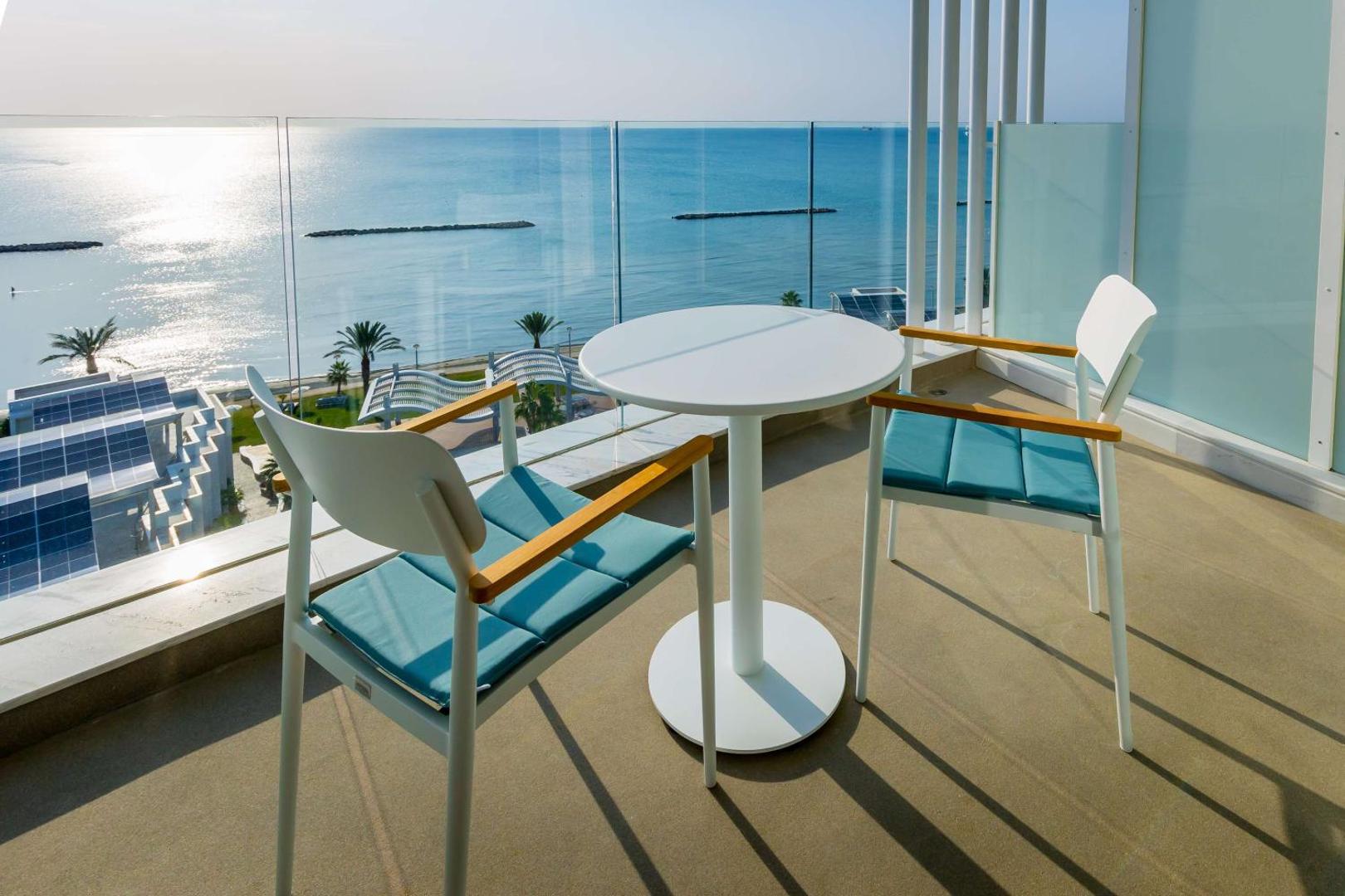 Radisson Beach Resort Larnaca numura balkons ar galdu, krēsliem un stikla margām, no kura paveras skats uz Vidusjūru