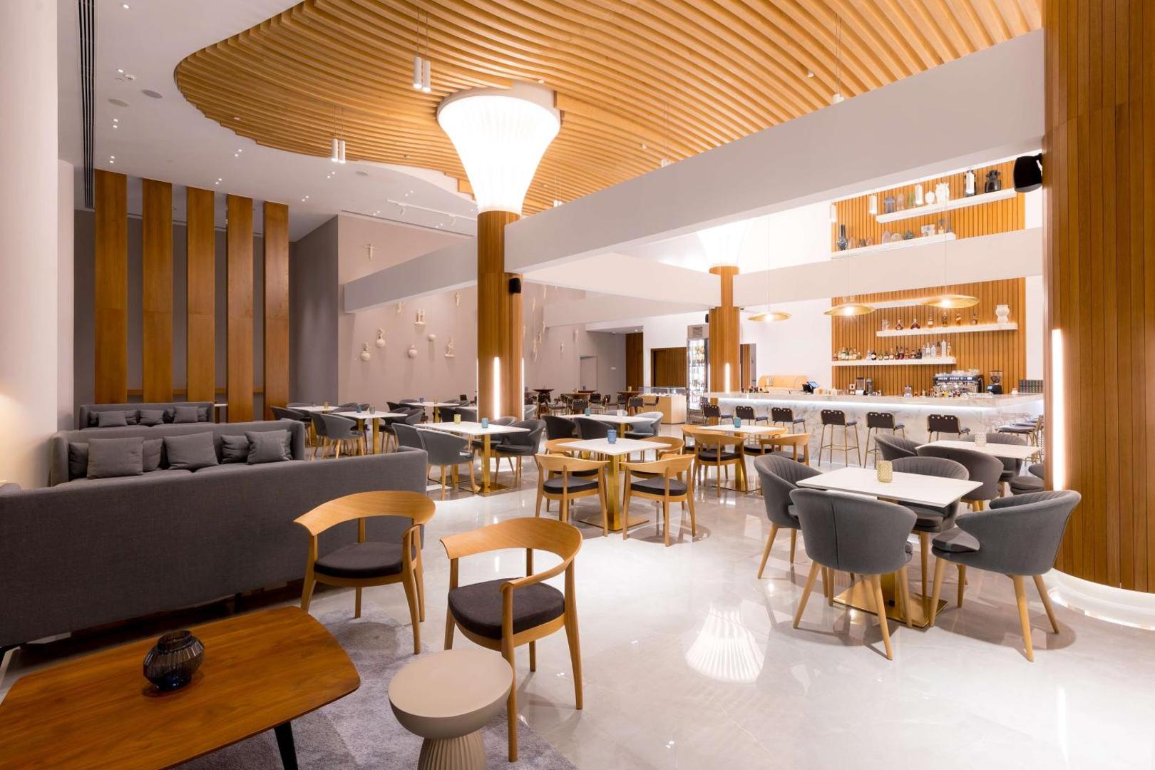 Plašs Radisson Beach Resort Larnaca lobby bārs un atpūtas zona ar gaišām mēbelēm, augstiem griestiem un koka apdares elementiem Kiprā.