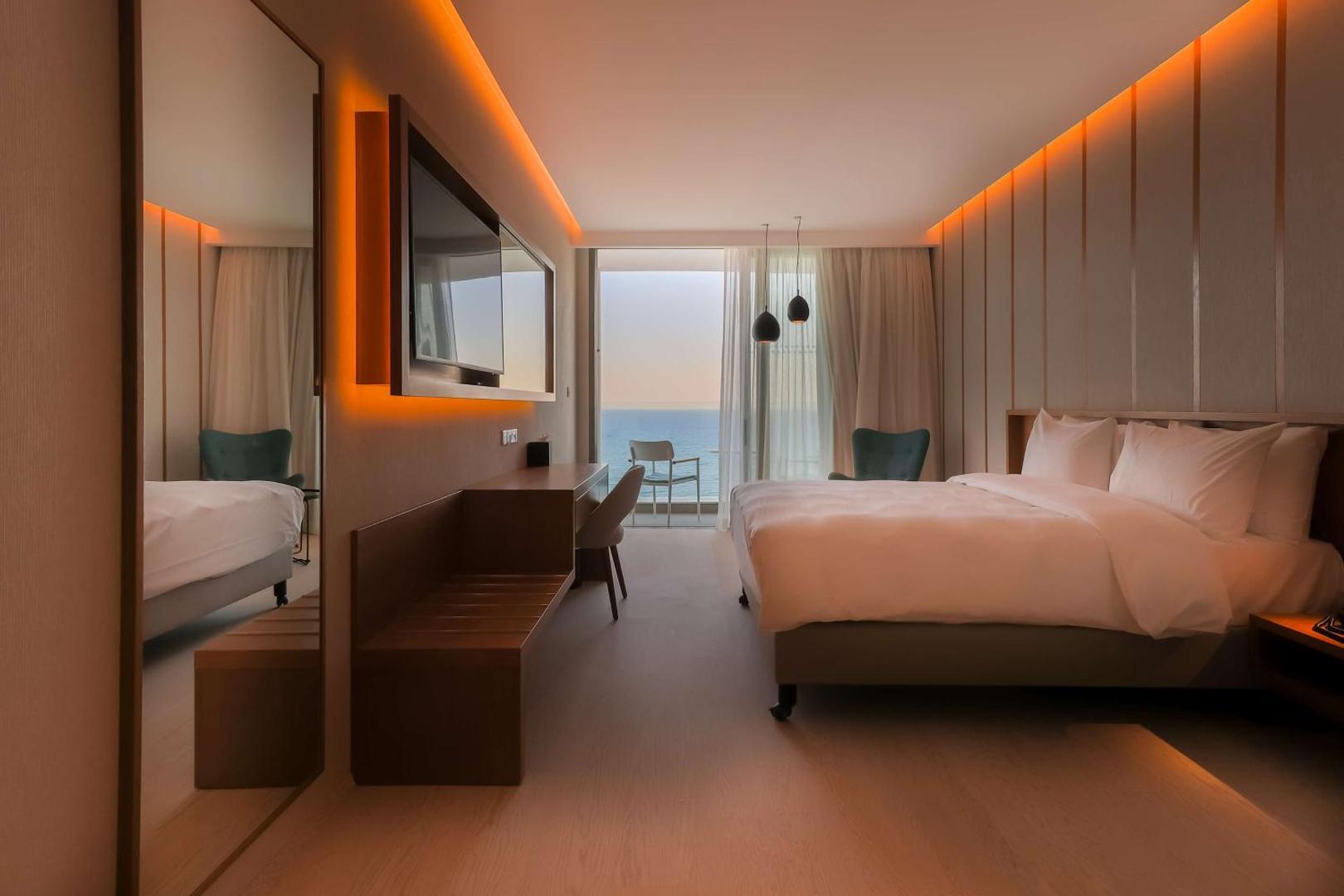 Radisson Beach Resort Larnaca moderns numurs ar skatu uz jūru, lielu gultu, sienas televizoru un siltu apgaismojumu Kiprā