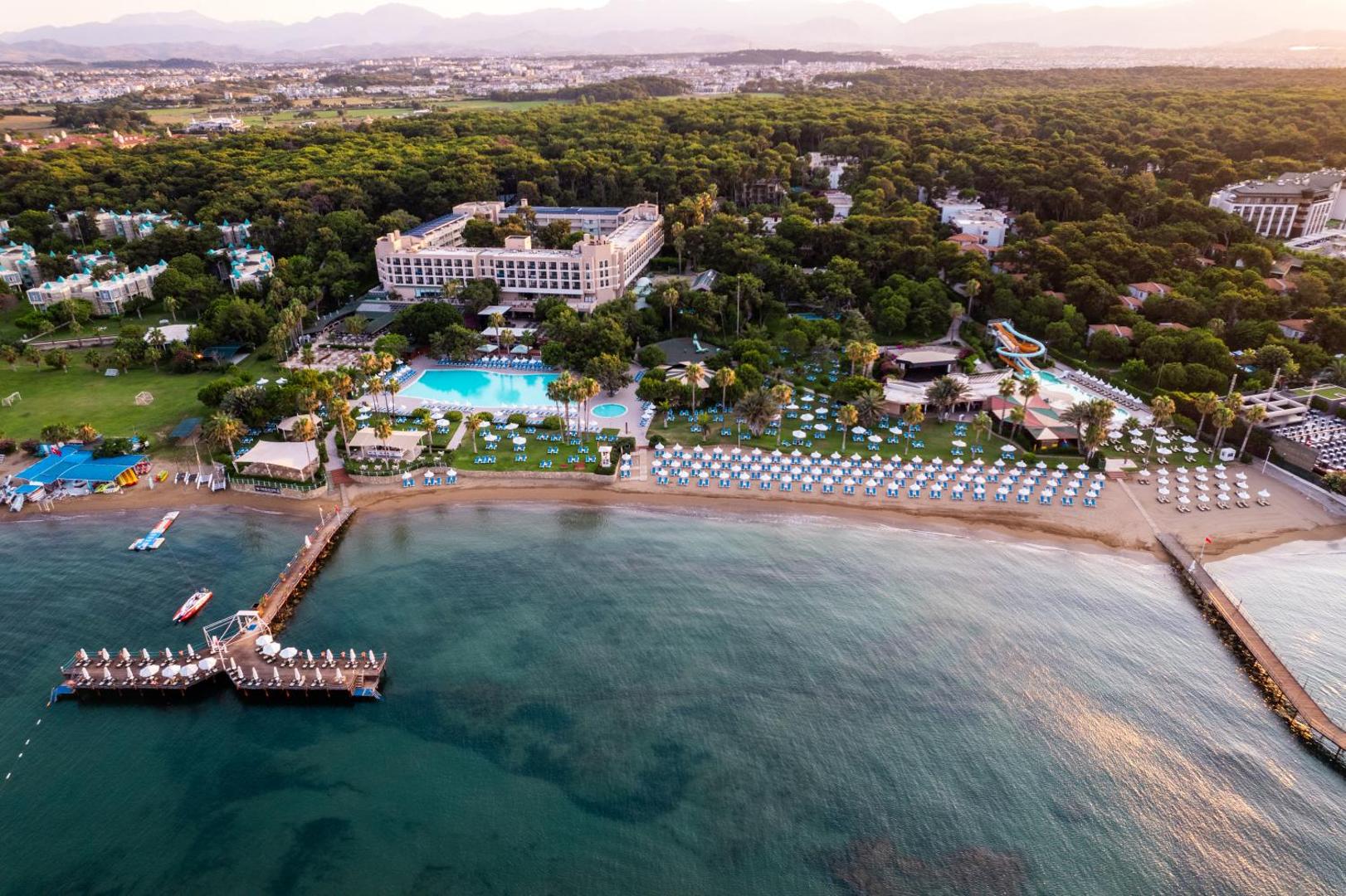 Turquoise Hotel Side aerofoto skats uz pludmali, piestātni un baseinu kompleksu priežu meža ielokā pie Vidusjūras Turcijā