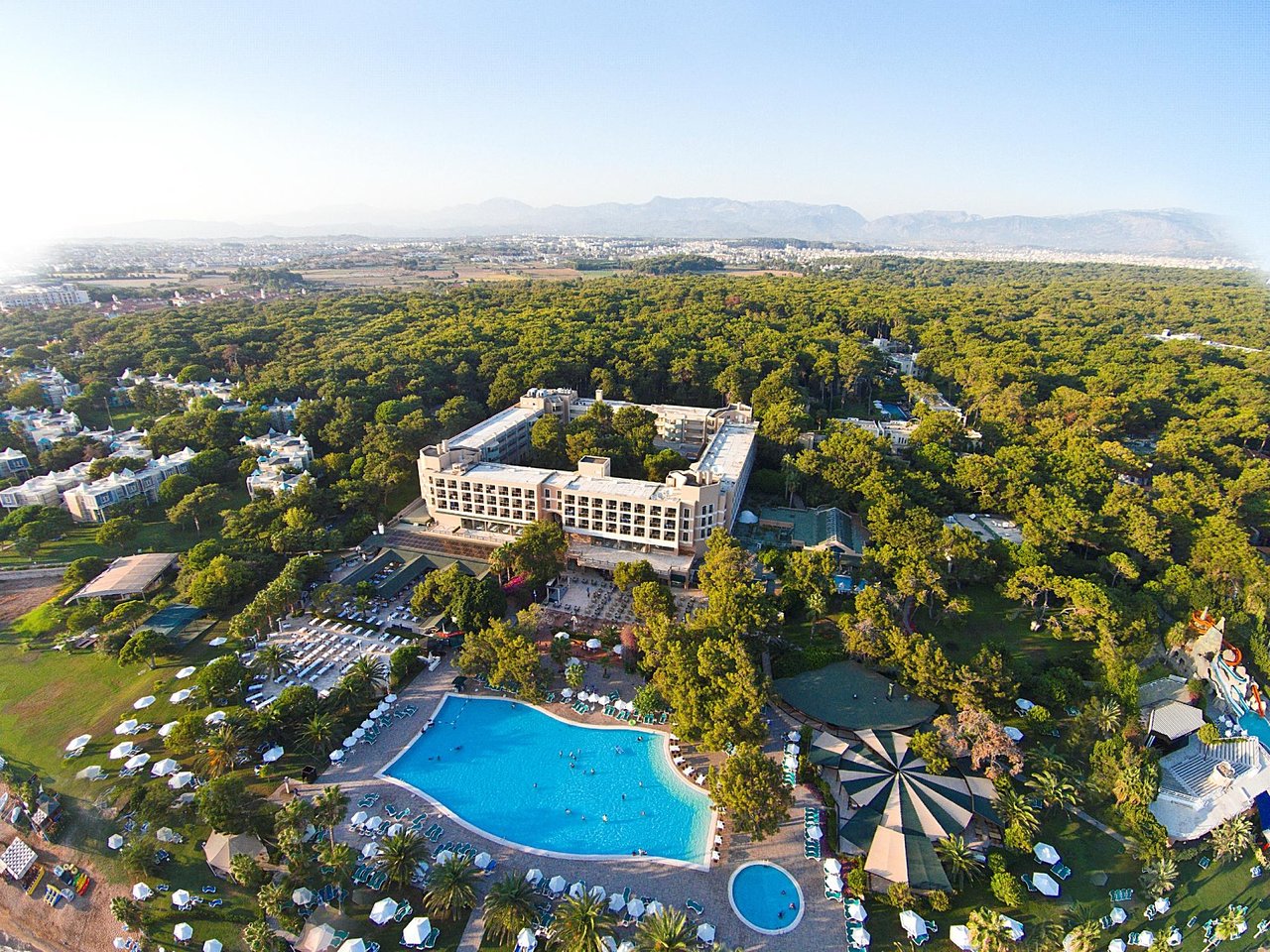 Turquoise Hotel lielais āra baseins un galvenā ēka dienas laikā, apkārtnē daudz zaļumu un atpūtas zonu