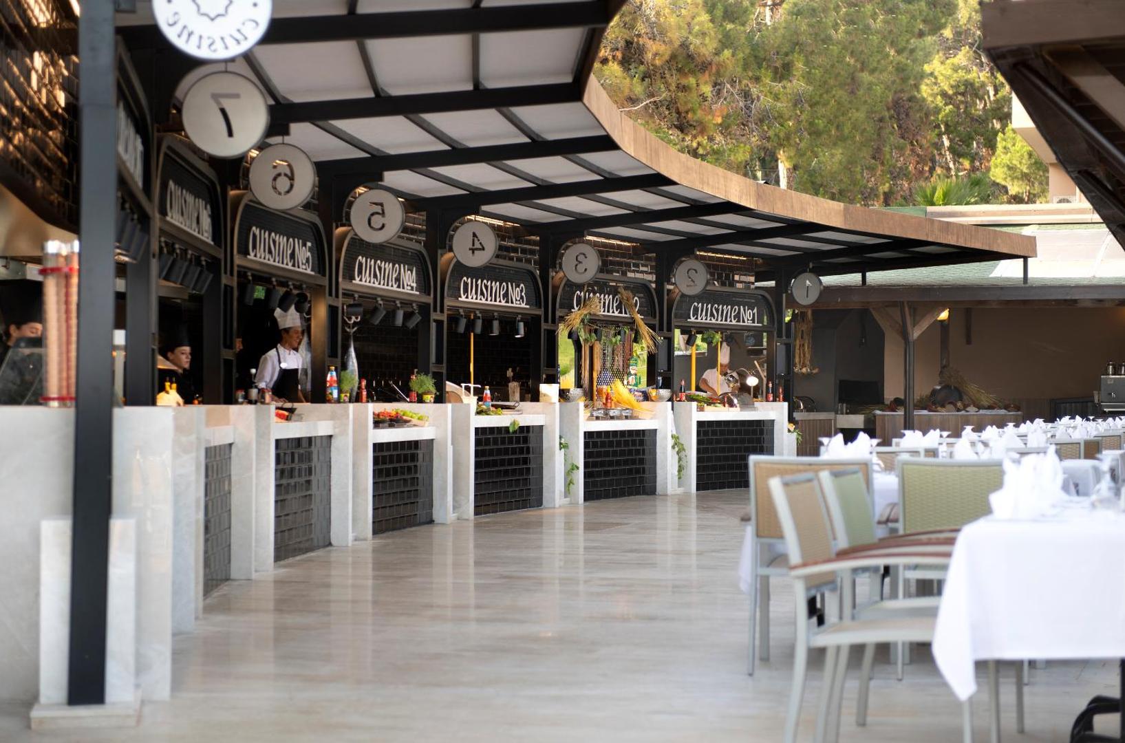 Turquoise Hotel bufetes zona ar dažādām ēdienu stacijām un pavāriem, kas gatavo viesu acu priekšā modernā interjerā.