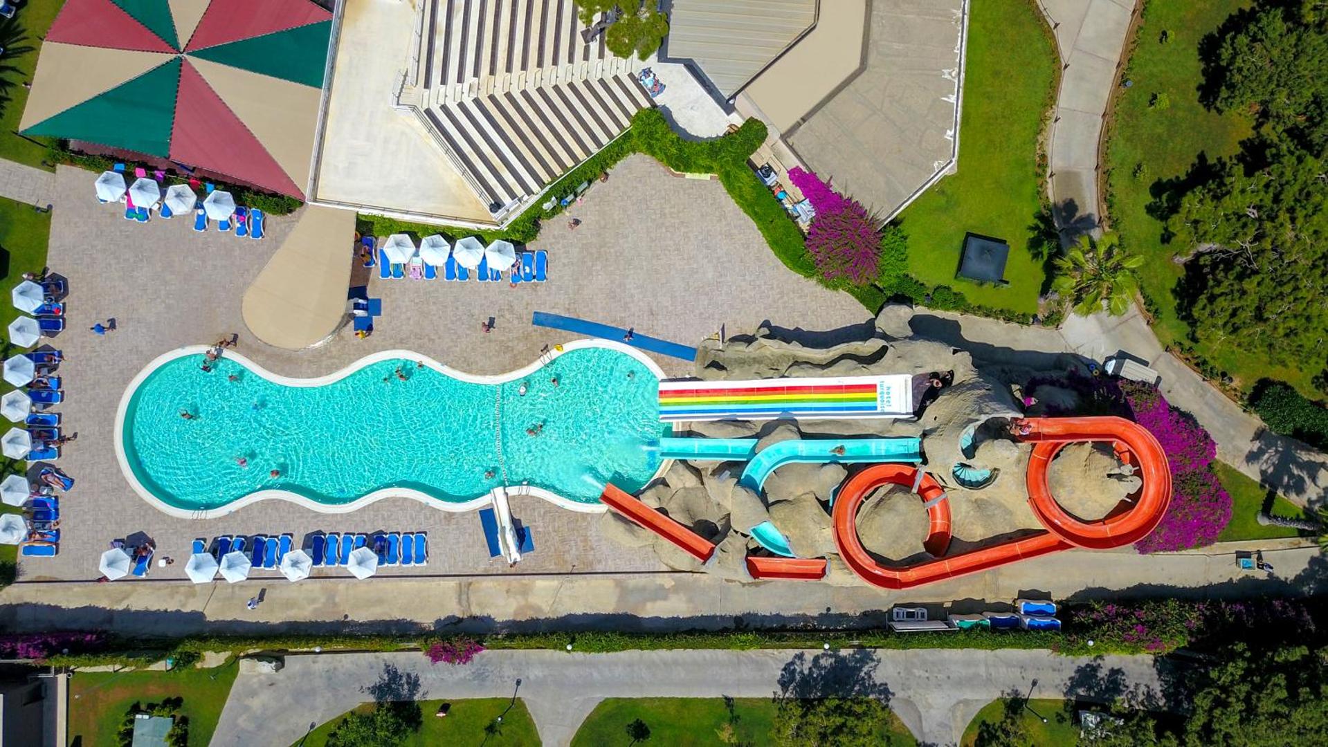 Turquoise Hotel akvaparks no putna lidojuma Sidē, Turcijā — baseins ar līkumotiem ūdens slidkalniņiem, sauļošanās krēsliem un amfiteātri blakus