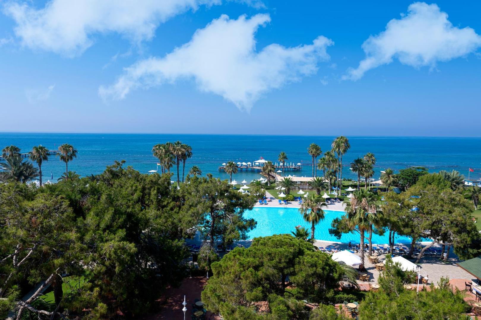 Turquoise Hotel skats no augšas uz zilo baseinu, zaļo dārzu un Vidusjūras piekrasti Sorgunā, Turcijā ar palmām un saulessargiem