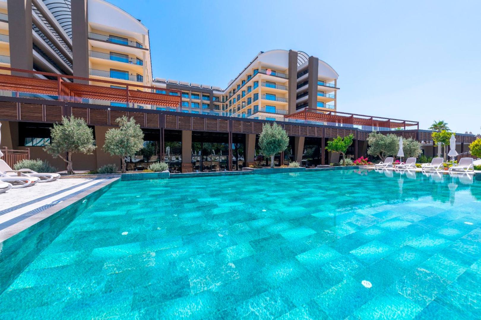 Sorgun Akadia Hotel Luxury baseina zona ar modernu arhitektūru un dekoratīviem kokiem — skats uz viesnīcas fasādi un terasēm