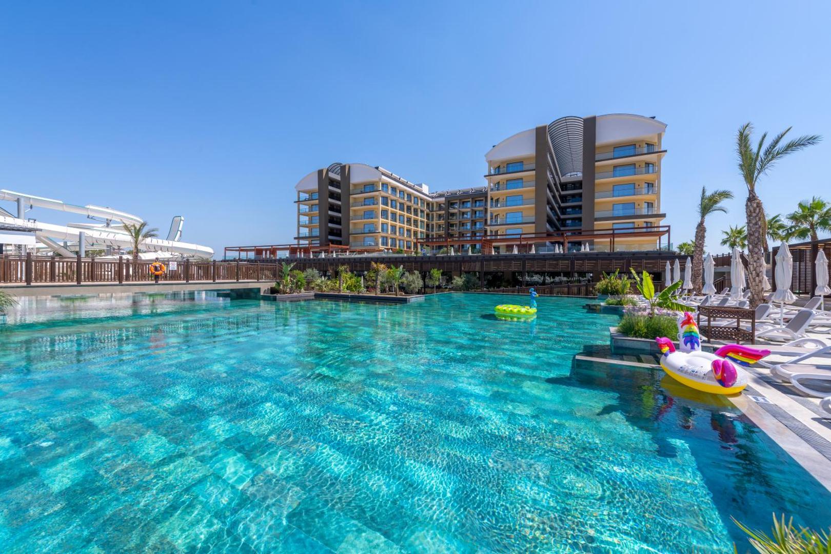 Sorgun Akadia Hotel Luxury āra baseins ar tirkīza ūdeni un viesnīcas ēku fonā — sauļošanās krēsli un palmas pie baseina malas