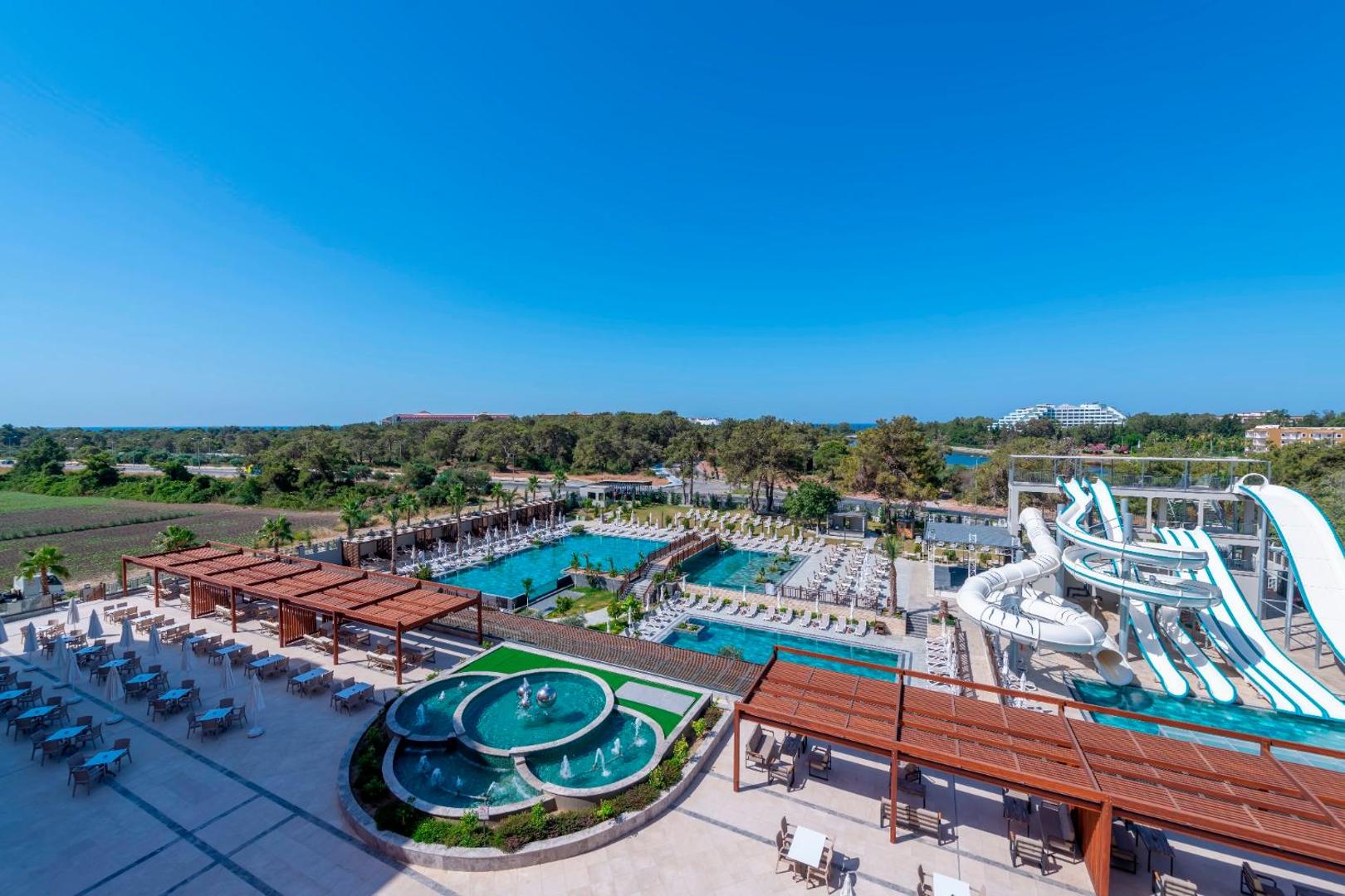 Sorgun Akadia Hotel Luxury teritorijas panorāmas skats ar strūklaku, akvaparku un baseiniem — apkārtnē zaļojoši koki un skats uz jūru