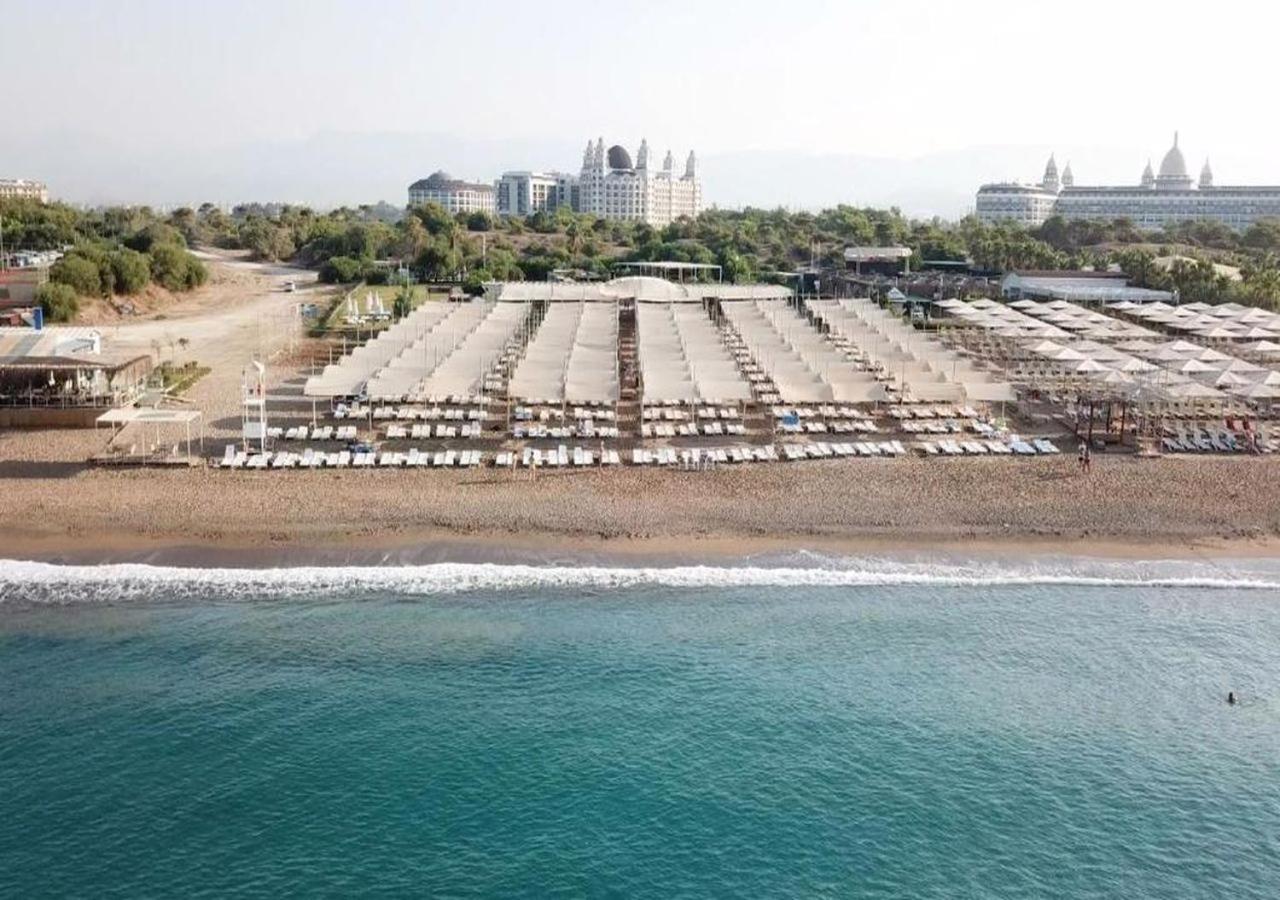 Sorgun Akadia Hotel Luxury privātā pludmale Sidē, Turcijā — plaša smilšu un oļu krasta līnija ar saulessargiem un zviļņiem