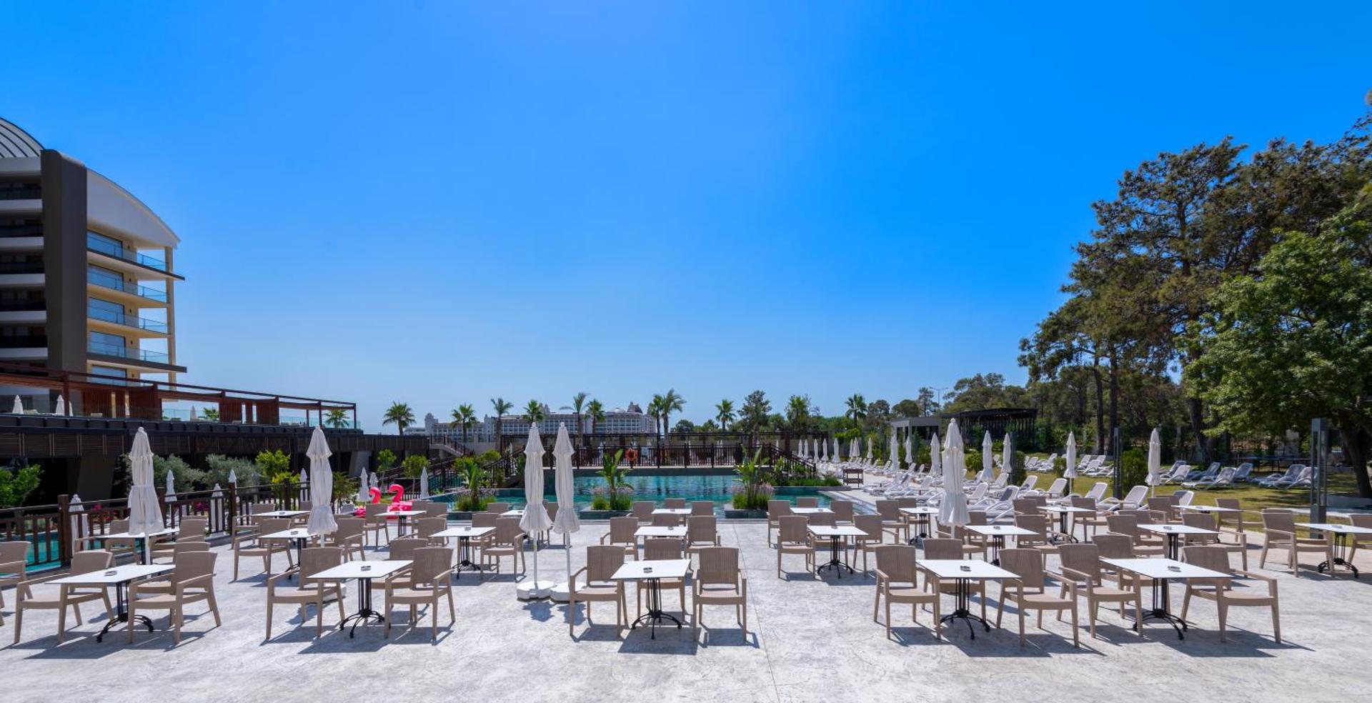 Sorgun Akadia Hotel Luxury āra baseina zona ar saulessargiem, galdiņiem un skatu uz viesnīcas ēku un apkārtnes priežu mežu