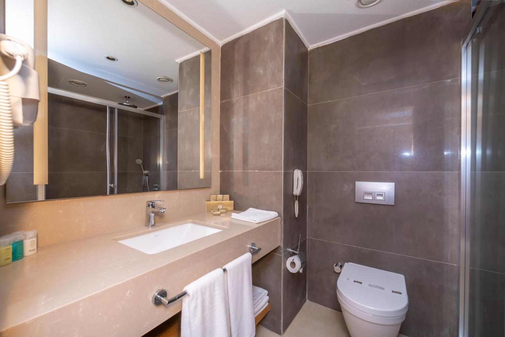 Sorgun Akadia Hotel Luxury numura vannas istaba ar modernu izlietni, lielu spoguli un dušu — mūsdienīgs dizains brūnos toņos