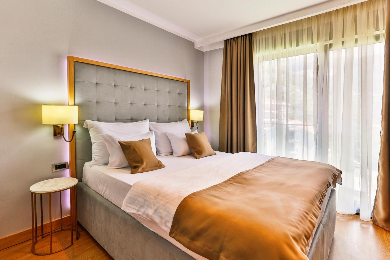 Hotel Lusso Mare viesnīcas numurs ar divguļamo gultu, mīkstu galvgali un gaišiem aizkariem pie lielā loga
