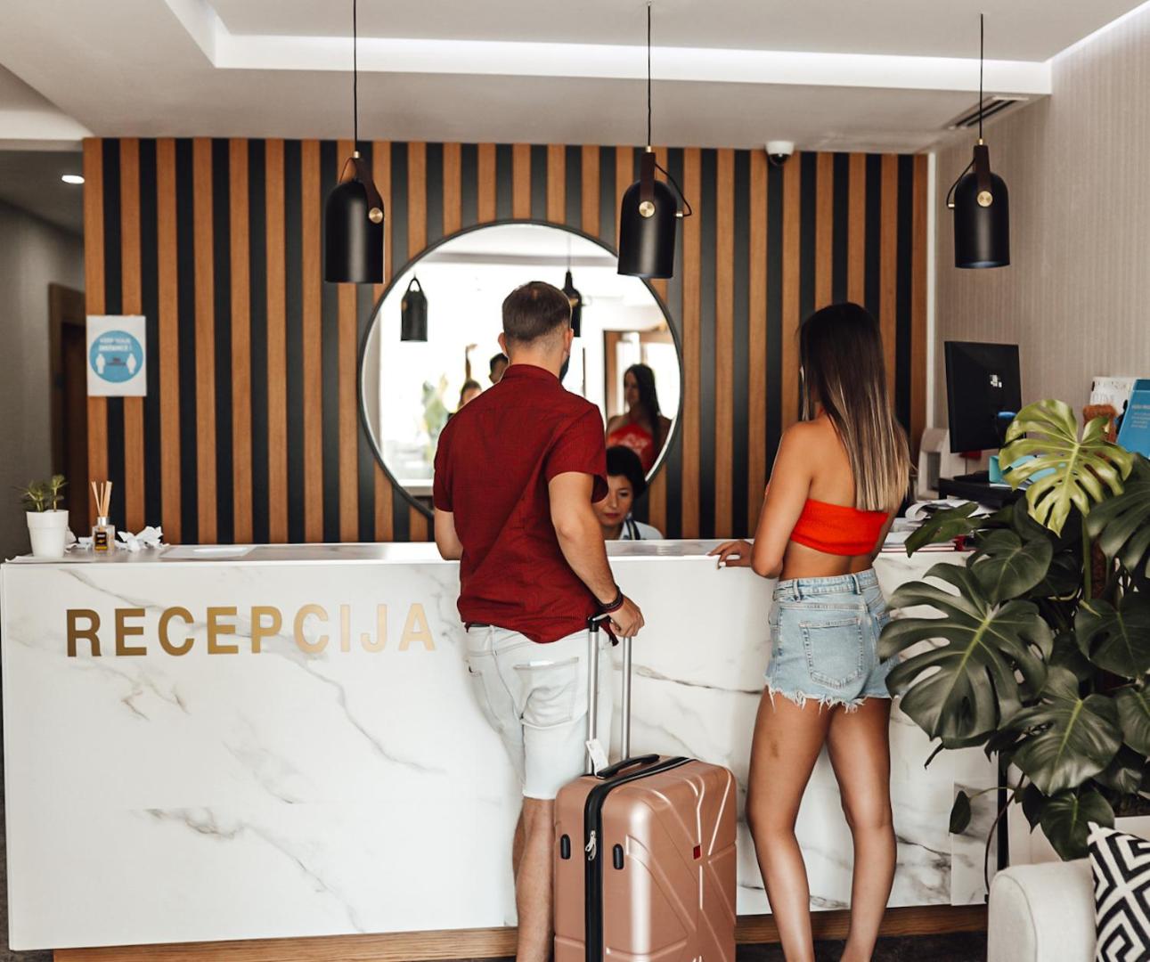 Viesu reģistrācija Hotel Lusso Mare recepcijā — moderns marmora lete un koka paneļu siena ar apaļu spoguli