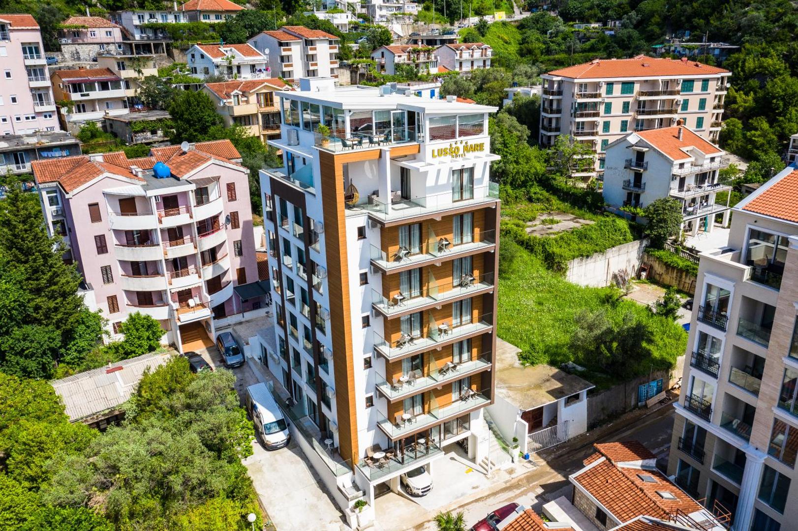 Hotel Lusso Mare ēkas skats no augšas Budvā, Melnkalnē — moderna arhitektūra ar balkoniem un jumta terasi pilsētas ainavā