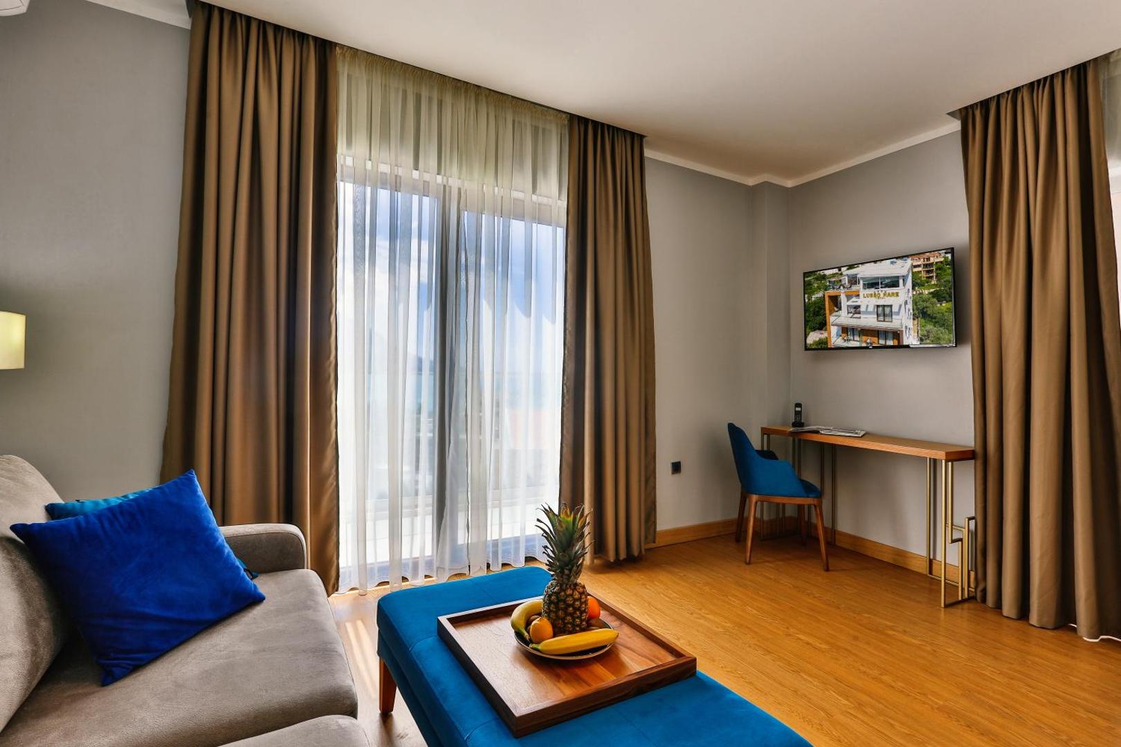 Hotel Lusso Mare numura dzīvojamā zona ar dīvānu, zilu pufu, darba galdu un TV pie sienas