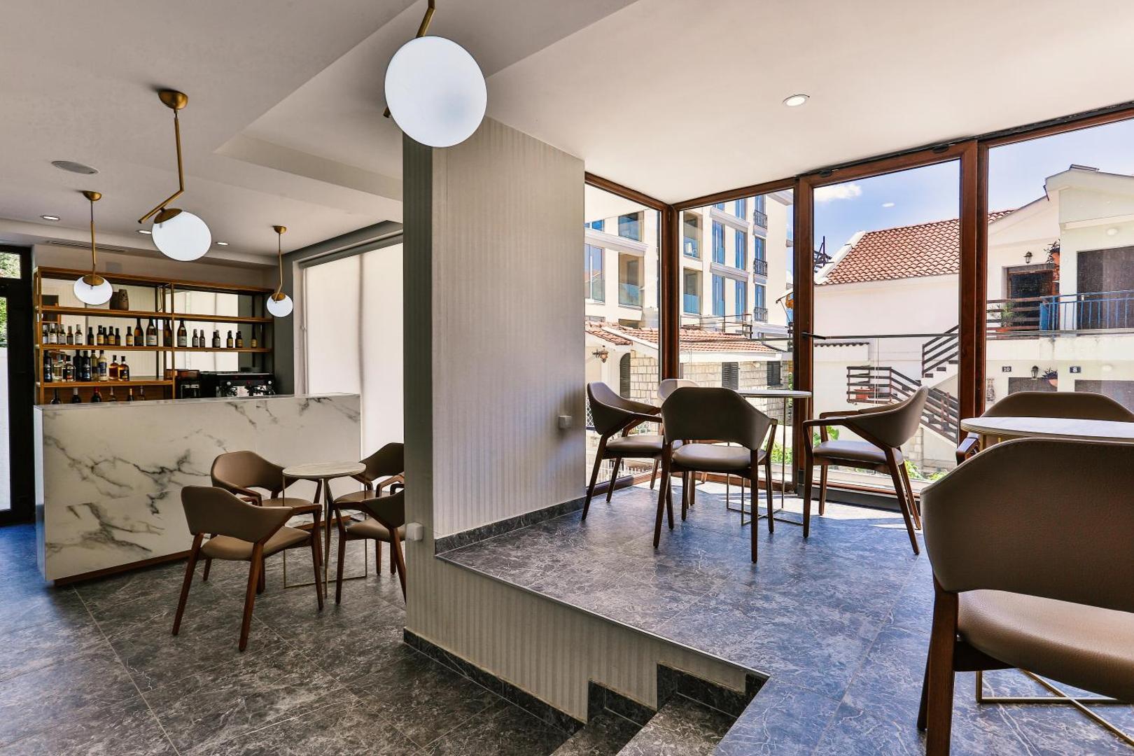 Hotel Lusso Mare gaišais vestibila bārs un atpūtas zona ar modernām mēbelēm, marmora leti un lieliem logiem Budvā, Melnkalnē