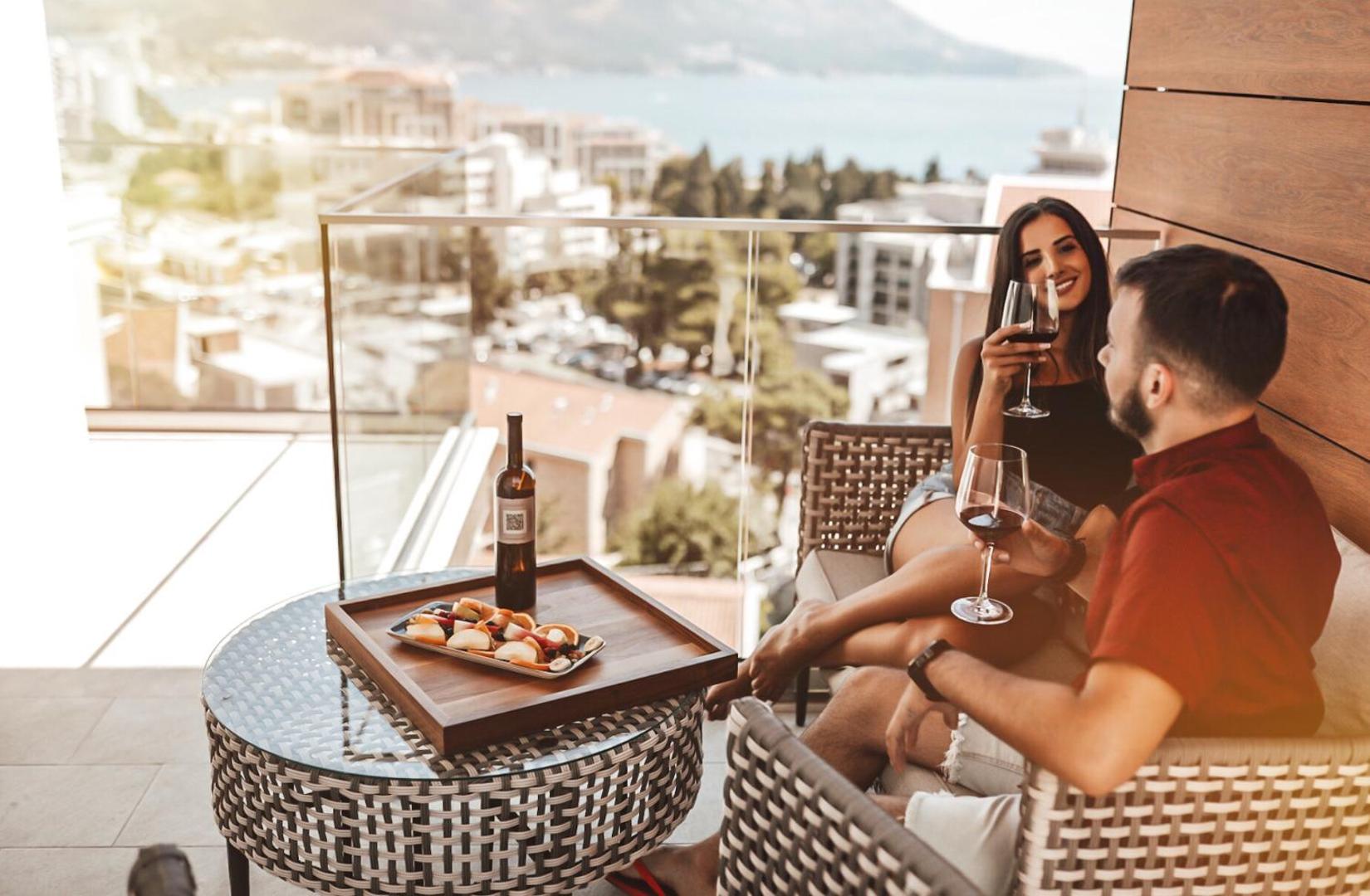 Hotel Lusso Mare numura balkons ar skatu uz pilsētu un jūru — pāris bauda vīnu un augļus saulrietā