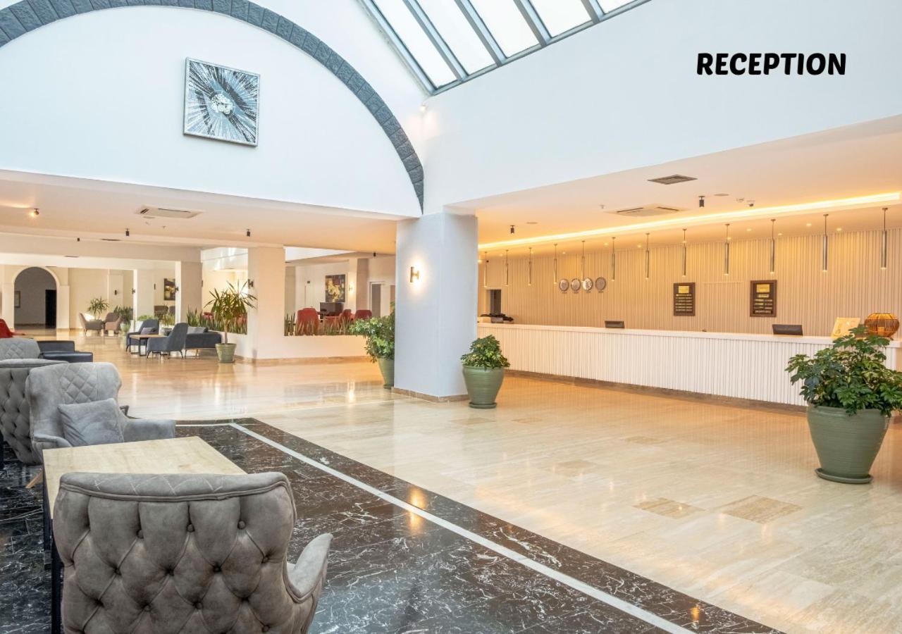 Kilikya Palace Goynuk viesnīcas recepcijas zona ar plašu gaišu zāli, marmora apdari, ērtiem atpūtas krēsliem un stikla jumtu