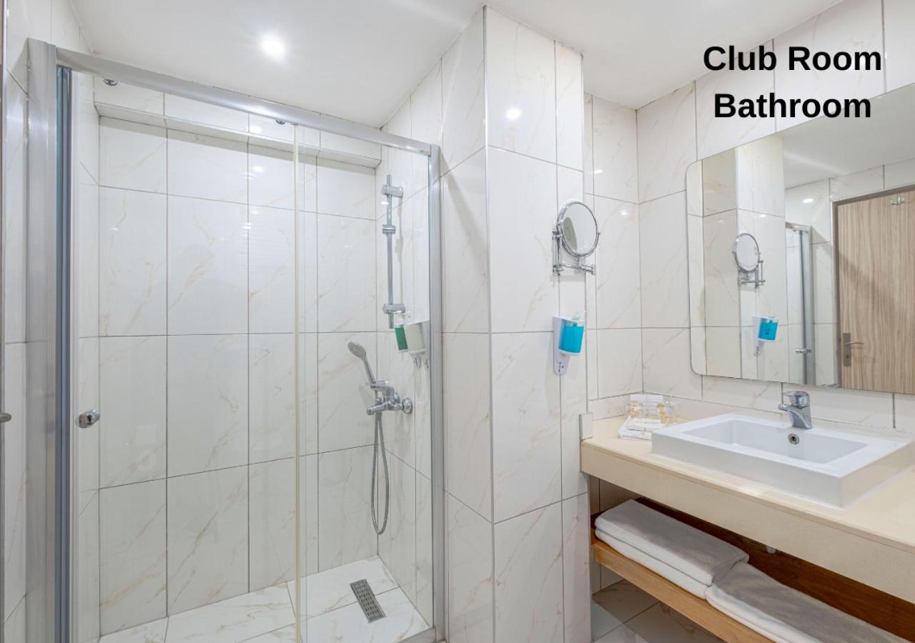 Kilikya Palace Goynuk Club numura vannas istaba ar gaišām flīzēm, stikla dušas kabīni un kompaktu izlietni