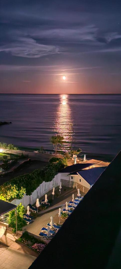 Nakts skats no Moonlight Hotel balkona uz mēness apspīdētu Melno jūru un viesnīcas apgaismoto āra terasi