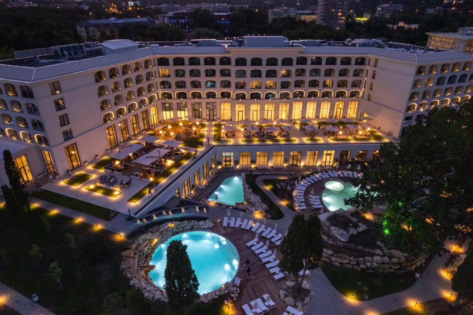 Aquahouse Hotel & SPA nakts skats uz izgaismoto fasādi un āra baseiniem Bulgārijā — eleganta arhitektūra ar siltu apgaismojumu un atpūtas zonām