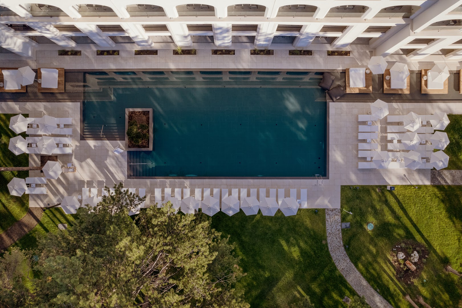 Aquahouse Hotel & SPA skats no augšas uz taisnstūra āra baseinu, baltiem saulessargiem un koptu zālienu priežu meža ielokā