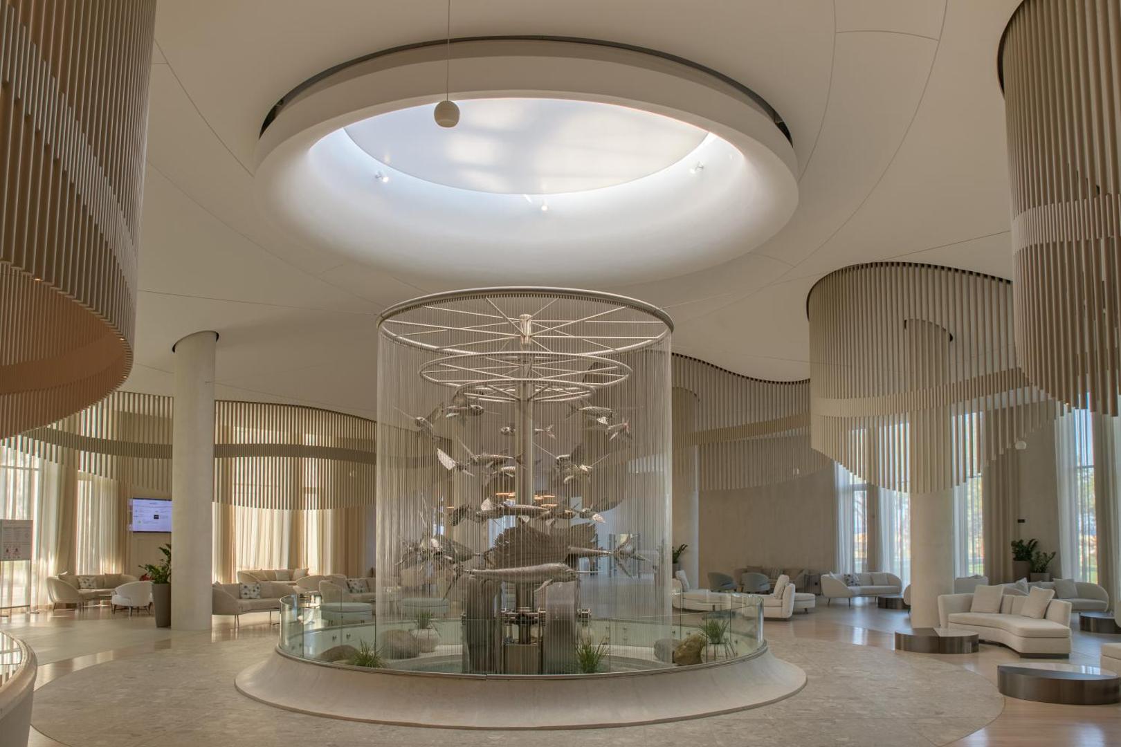 Aquahouse Hotel & SPA plašais vestibils ar unikālu centrālo ūdens instalāciju, gaišām mēbelēm un augstiem griestiem