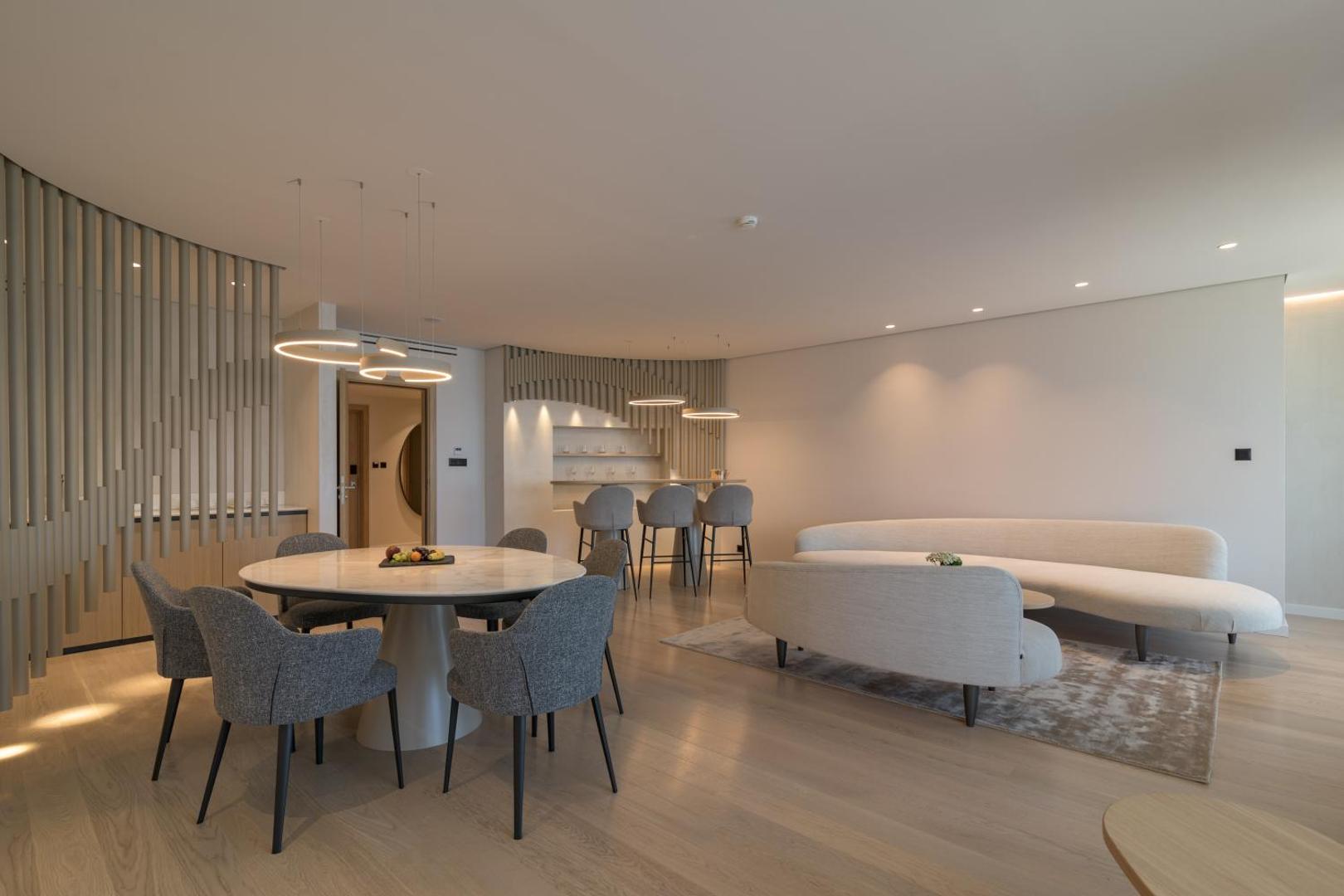 Aquahouse Hotel & SPA luksusa numura dzīvojamā zona ar apaļu pusdienu galdu, modernu dīvānu un bāra leti