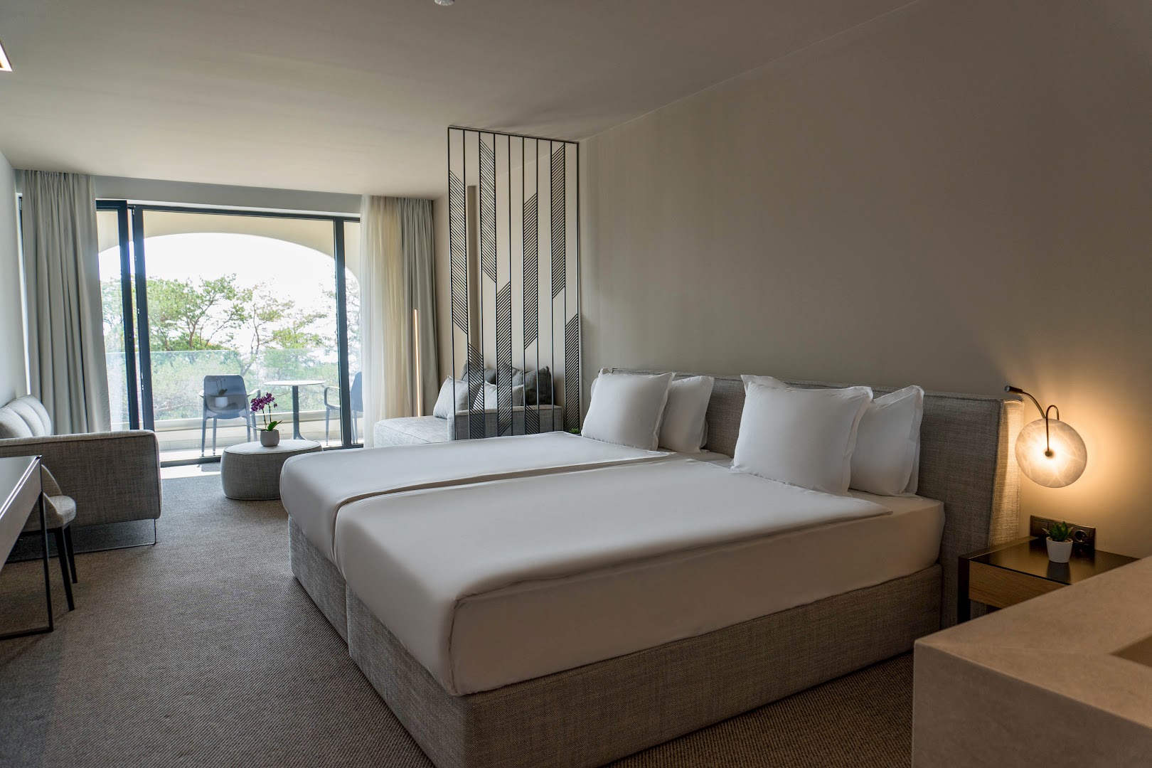 Gaišs Aquahouse Hotel & SPA numurs ar lielu gultu, atpūtas stūri un izeju uz balkonu ar skatu uz priežu mežu
