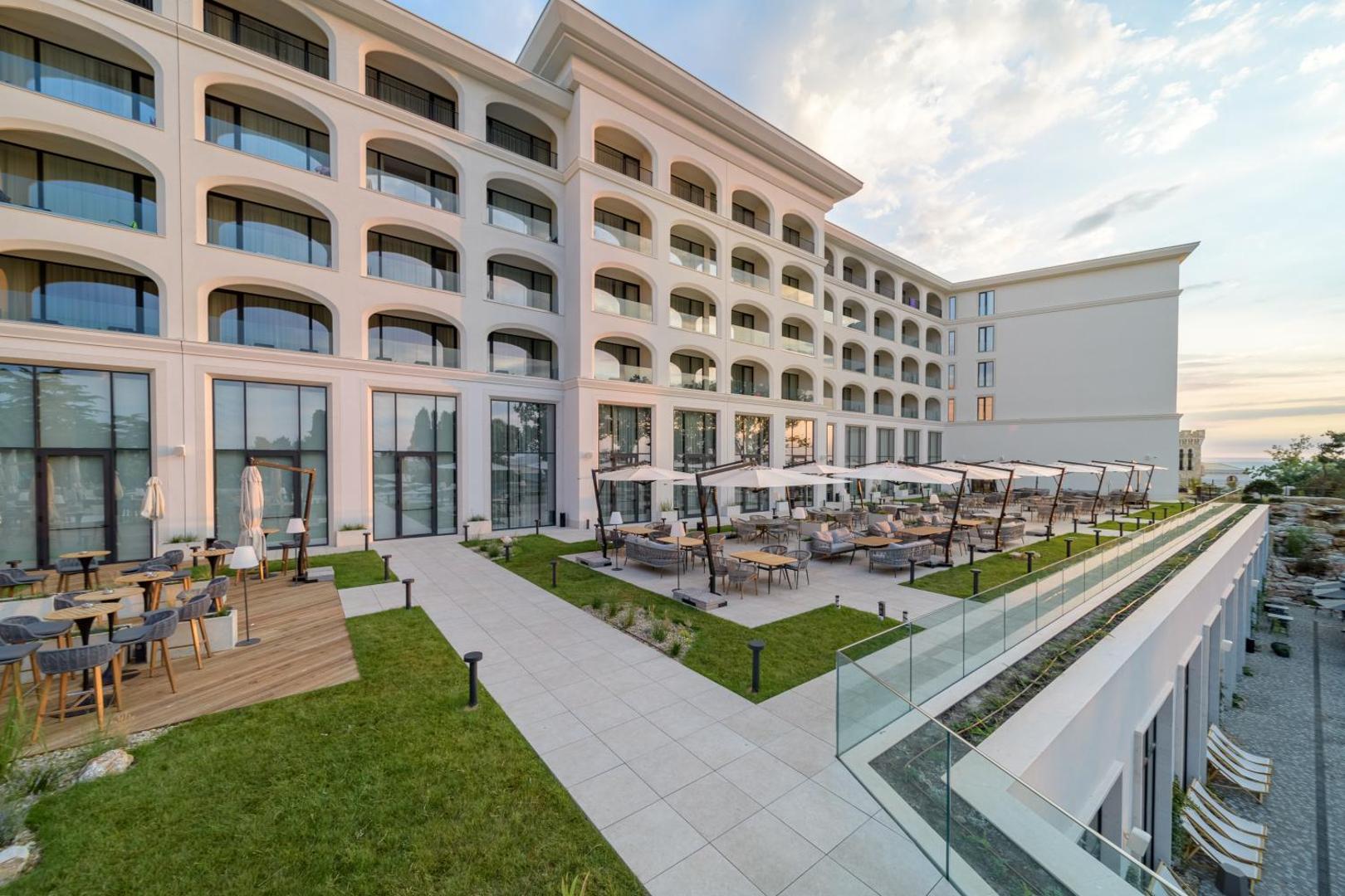 Aquahouse Hotel & SPA āra terase ar galdiņiem un dīvāniem pie viesnīcas fasādes, skats uz jūras pusi vakara gaismā